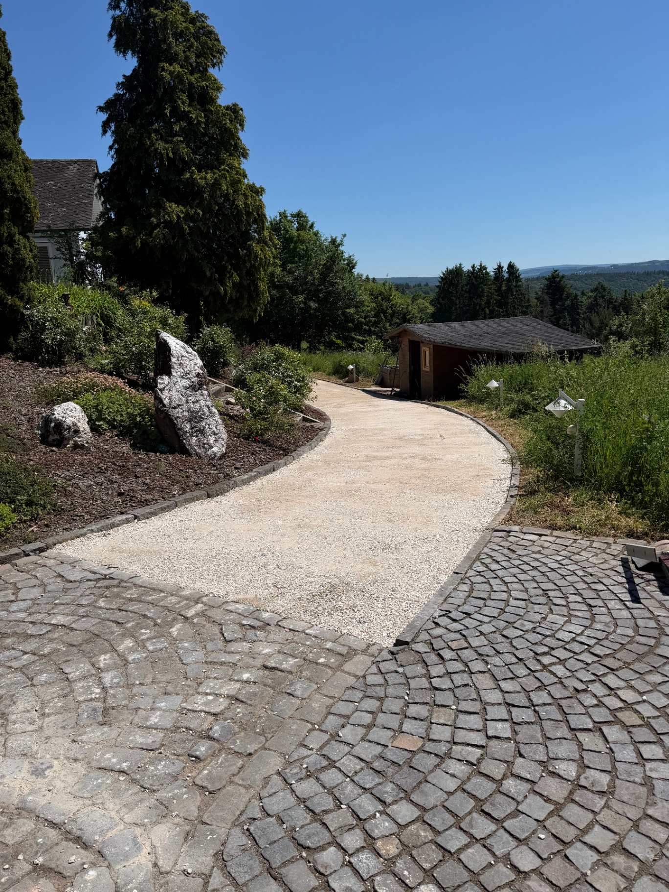 Neu gepflasterte Hofeinfahrt mit Naturstein-Kopfsteinpflaster und Schotterweg im Garten